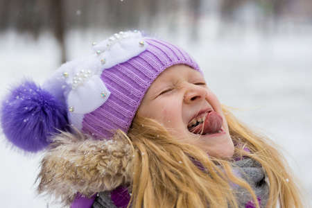 smiling little girl catching a snowflakes with her tongueの写真素材
