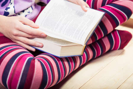 girl sitting on a wooden floor and reading a bookの写真素材