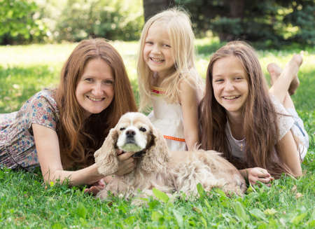 smiling mother with her daughters and dog on a grassの写真素材