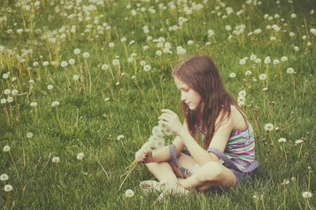 young blonde girl with bunch of dandelions on a green lawnの写真素材