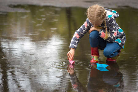 girl runs the pink paper boat in a puddle in the rain, springの写真素材
