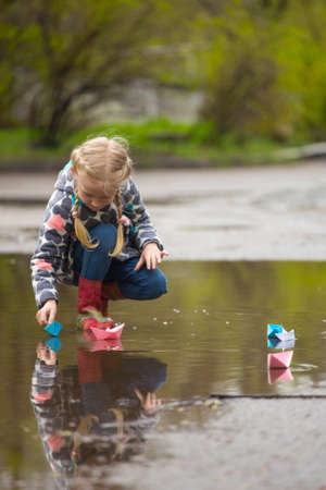 Girl runs the pink paper boat in a puddle in the rain, springの写真素材