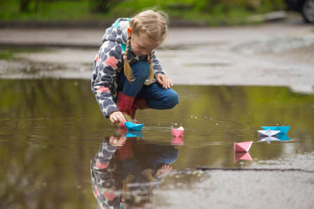 Girl runs the pink paper boat in a puddle in the rain, springの写真素材
