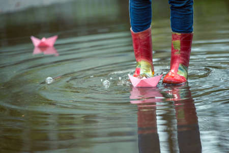 Girl runs the pink paper boat in a puddle in the rain, springの写真素材