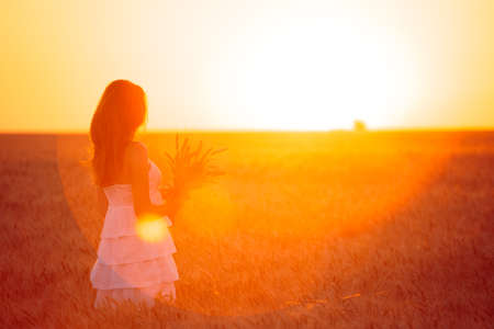 young girl joys on the wheat field at the sunset timeの写真素材