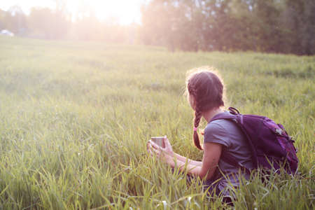 girl hiker sitting on a meadow grass and enjoying a sunsetの写真素材