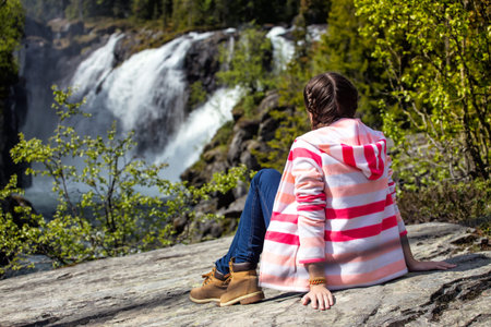 girl hiker sitting on a rock and a waterfall Rjukandefossen in the background, Norwayの写真素材