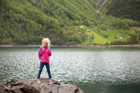 little girl tourist with a backpack standing on the shore of the lake and mountains in the background, Norwayの写真素材