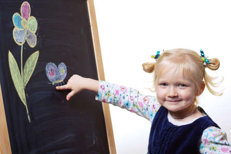 smiling little girl standing near blackboard on which are painted flower and butterflyの写真素材