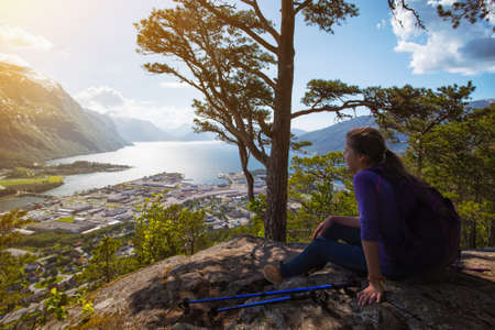 Rampestreken. girl hiker with a backpack and trekking pole sitting and looking on Romsdalsfjorden and Andalsnes, Norwayの写真素材