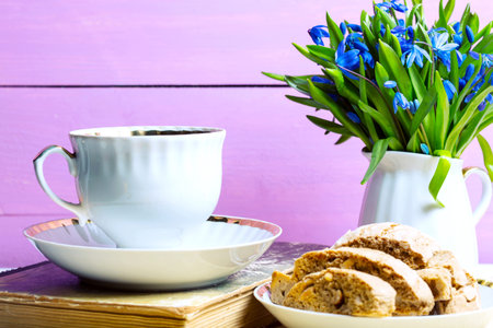 snowdrops in a vase, a cup of tea and biscotti on the tableの写真素材