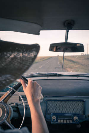young girl driving a retro car by the road at the fieldsの写真素材