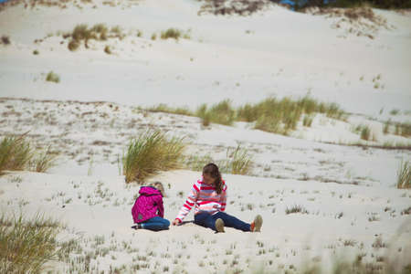 girls sisters sitting in the sand on the sand dunes and blue sky in the background,  baltic seaの写真素材