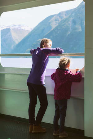 Two girls standing on the ferry and look out the window, mountains in the background, Norwayの写真素材