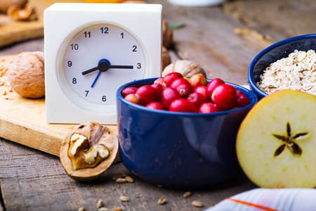healthy breakfast - clock, milk, oatmeal, cranberries, nuts, apples on a wooden tableの写真素材