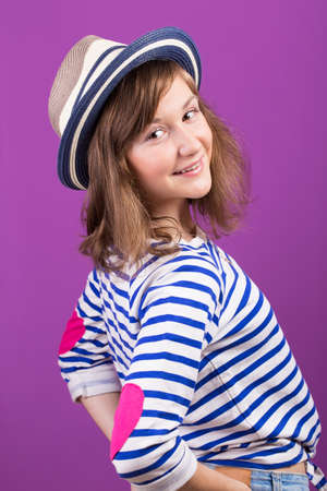 beautiful smiling teen girl in a hat posing on a purple backgroundの写真素材