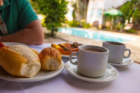 Breakfast - two cups of coffee, rolls and papaya on the pool backgroundの写真素材