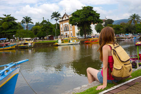Tourist girl sitting on the dock with colorful boats in the bay of the famous historical town Paraty, Brazilの写真素材