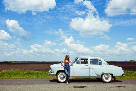 girl stands near a retro car, the background field, and a bright blue skyの写真素材