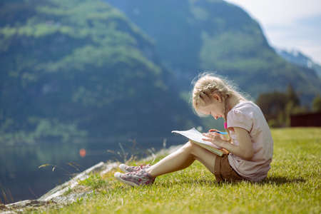 girl sitting and draws on the bank, norwayの写真素材