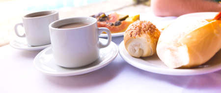 Breakfast traveler - two cups of coffee, rolls and papaya on the pool backgroundの写真素材