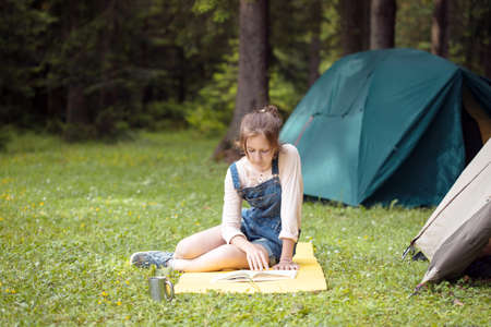 girl hiker sitting and reading a book near the tentの写真素材