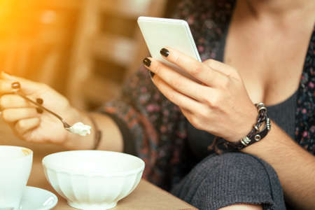 breakfast - girl sitting with smartphone and a cup of coffee and dessertの写真素材