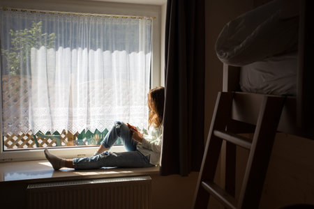 teen girl sitting on a windowsill with a smartphone in the children's room