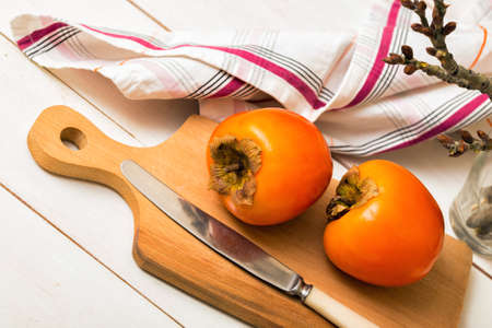 healthy food. Two persimmons are on the board, a knife and a towelの写真素材