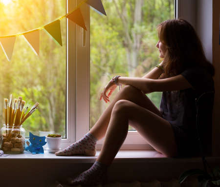 teen girl sitting on a windowsill in the children's roomの写真素材