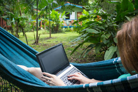 girl lying in a hammock and working on a laptop at the gardenの写真素材