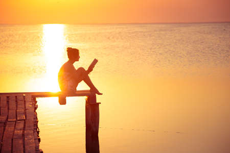 girl sitting on a pier and reading at the sunset timeの写真素材