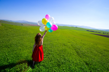 Happy girl in the meadows tuscan with colorful balloons, against the blue sky and green meadow. Tuscany, Italyの写真素材