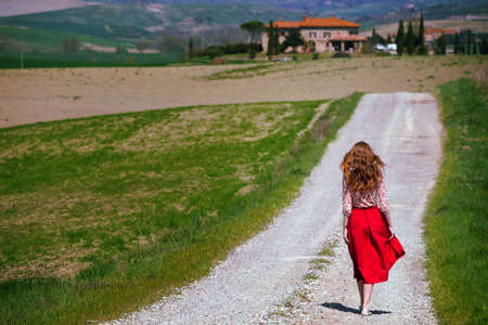 girl is walking along the road among the fields and a typical Tuscan landscape behind her. Tuscany, Italyの写真素材