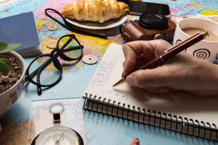 Plan of trip. background - what to take for a trip. Women's hands and notepad for writing ideas, map, retro camera, money, coins, croissant, coffee, pen, compass, sunglasses, smartphoneの写真素材