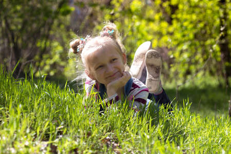 blonde little girl lies on the grass outdoorsの写真素材