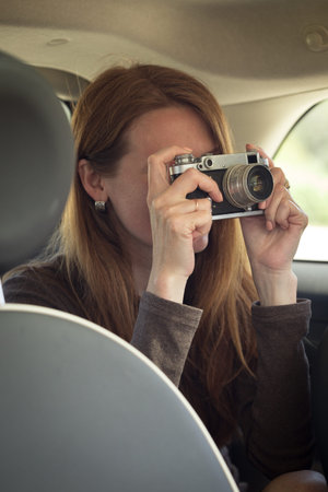 Girl with retro camera taking pictures at thr car. Photo taken through glass