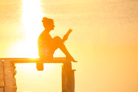 girl sitting on a pier and reading at the sunset timeの写真素材