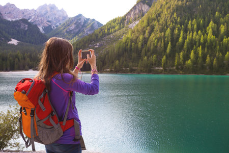 girl hiker taking a photo on a smartphone at the Braies lake, Dolomites Italy