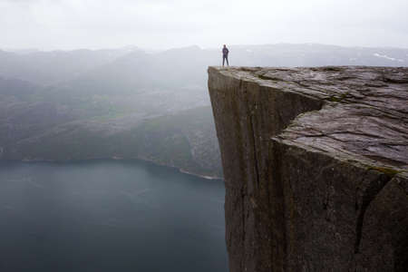 happy girl hiker standing on Preikestolen and looking at the mountains in overcast day, Preikestolen -famous cliff at the norwegian mountainsの写真素材