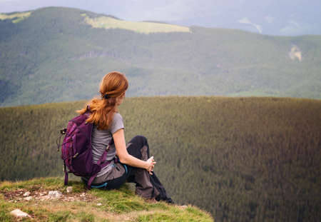 girl hiker with a backpack sitting on the background of mountains and forests. Vorokhta - Ukrainian landscape.の写真素材