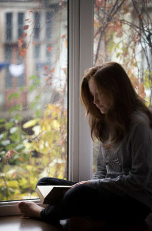 teen girl sitting on a windowsill with a book  in the children's roomの写真素材