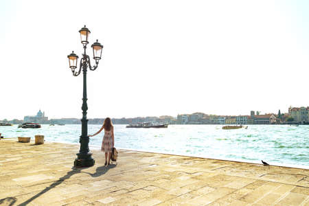 The girl is standing near streetlight on the waterfront near the grand canal in Venice. Italyの写真素材