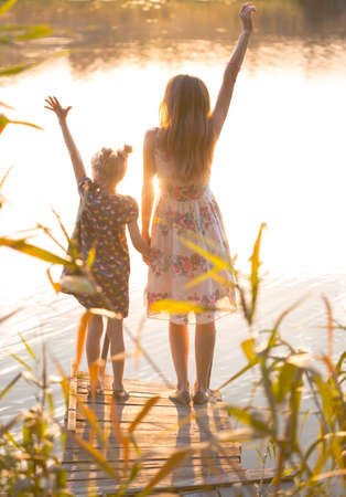 happy family - mother and daughter standing on the pier in sunset lightの写真素材