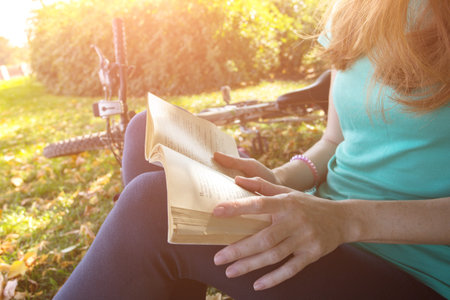 girl in the park sits under a tree and reads a book. next to it there is a bicycle and a backpackの写真素材