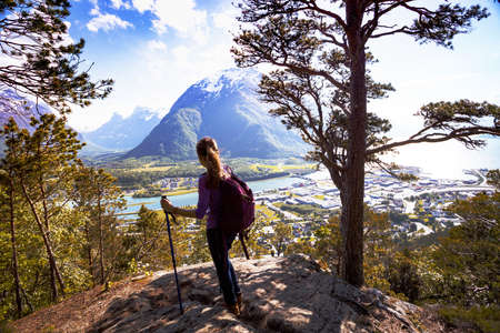 Rampestreken - girl hiker with a backpack and trekking pole standing and looking on Romsdalsfjorden and Andalsnes, Norwayの写真素材