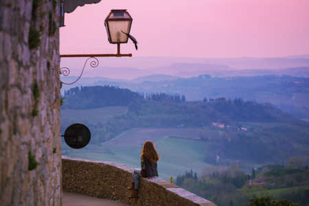 San Gimignano. girl looking at the tuscanian landscape with the hills and cypresses at dawnの写真素材