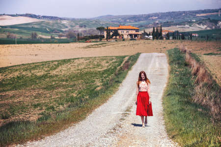 girl is walking along the road among the fields and a typical Tuscan landscape behind her. Tuscany, Italyの写真素材