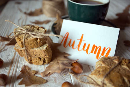 Beautiful autumn background - cup of tea, biscotti, autumn leaves and inscription Autumnの写真素材