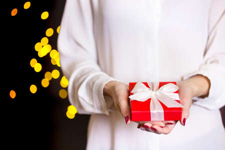 girl holding beautiful  gift for the day valentines day. red box and white bow and bokeh in the background
の写真素材